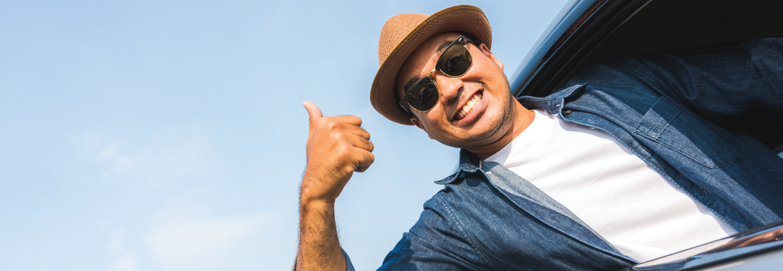 Man with hat and sunglasses leaning out of the car with thumb up