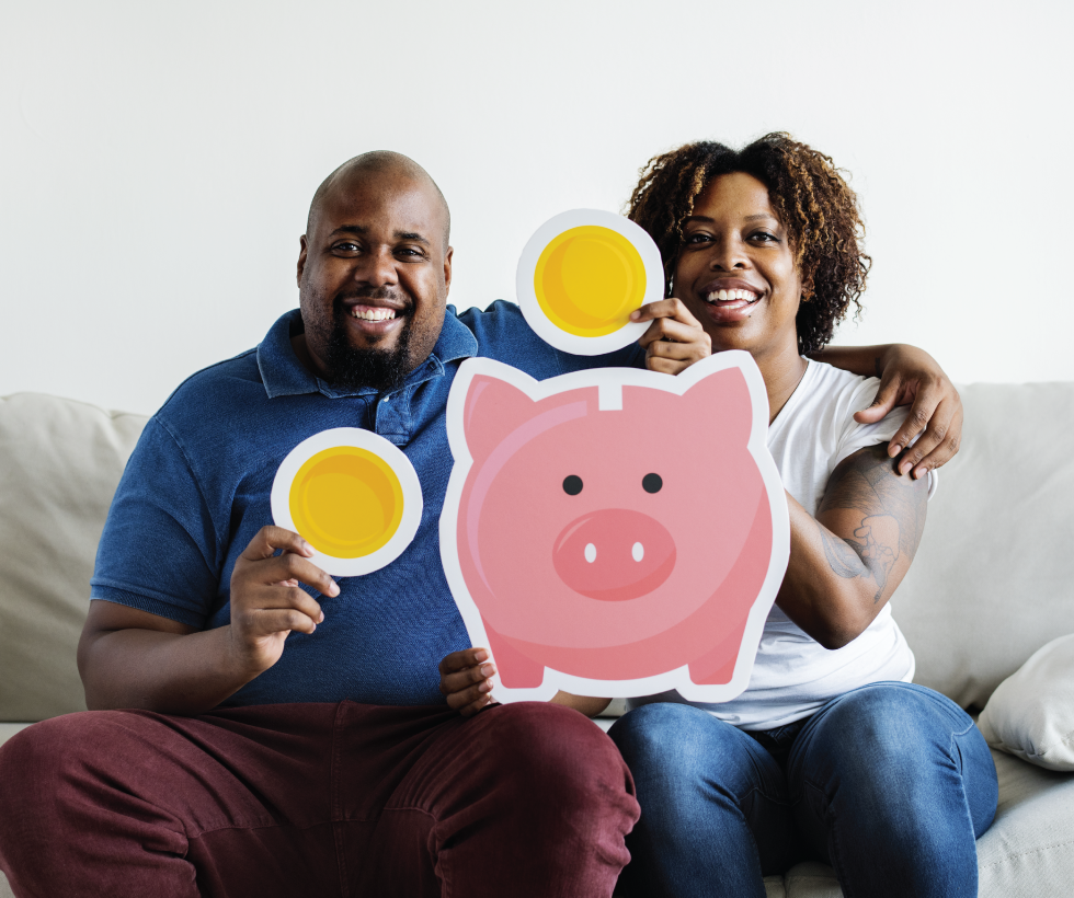 couple on couch holding paper coins and paper piggy bank