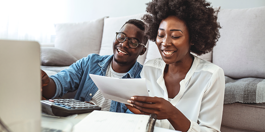 A couple on a sofa looking at a document together with a laptop open in front of them.