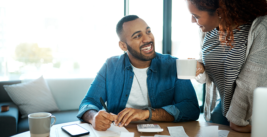 A couple going over paperwork at a table with a calculator and cups of coffee.