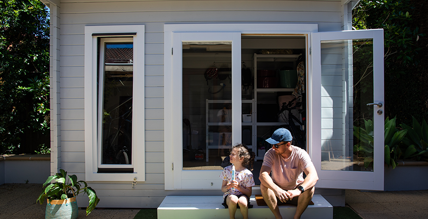 A small backyard accessory dwelling unit with glass doors, an adult and child sitting on the step outside.