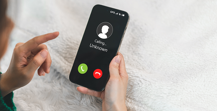 A hand reaching toward a phone showing an incoming call from an unknown caller.