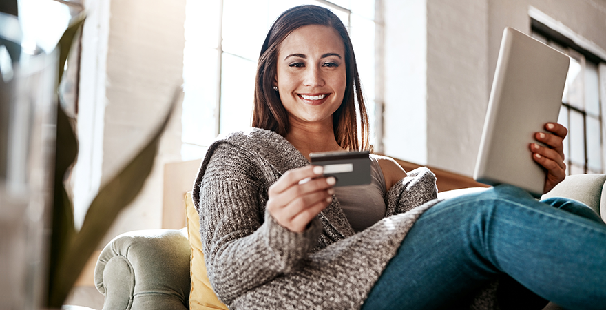 A woman sitting on a sofa with a laptop, holding a credit card.