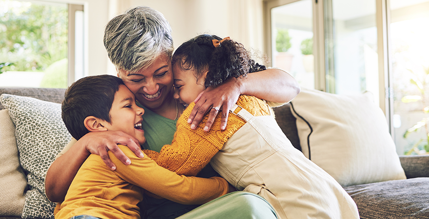 An older woman hugging two grandchildren on a sofa.