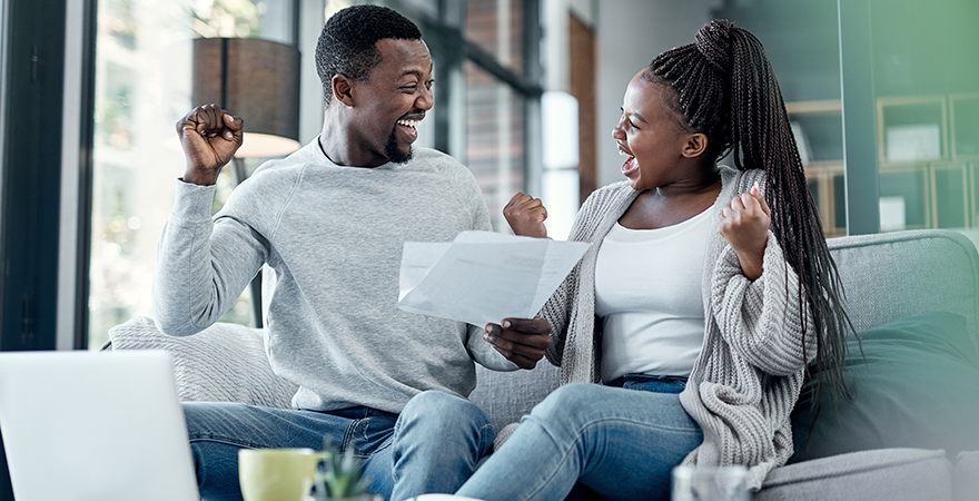 A couple on a sofa celebrating as they read a document together.
