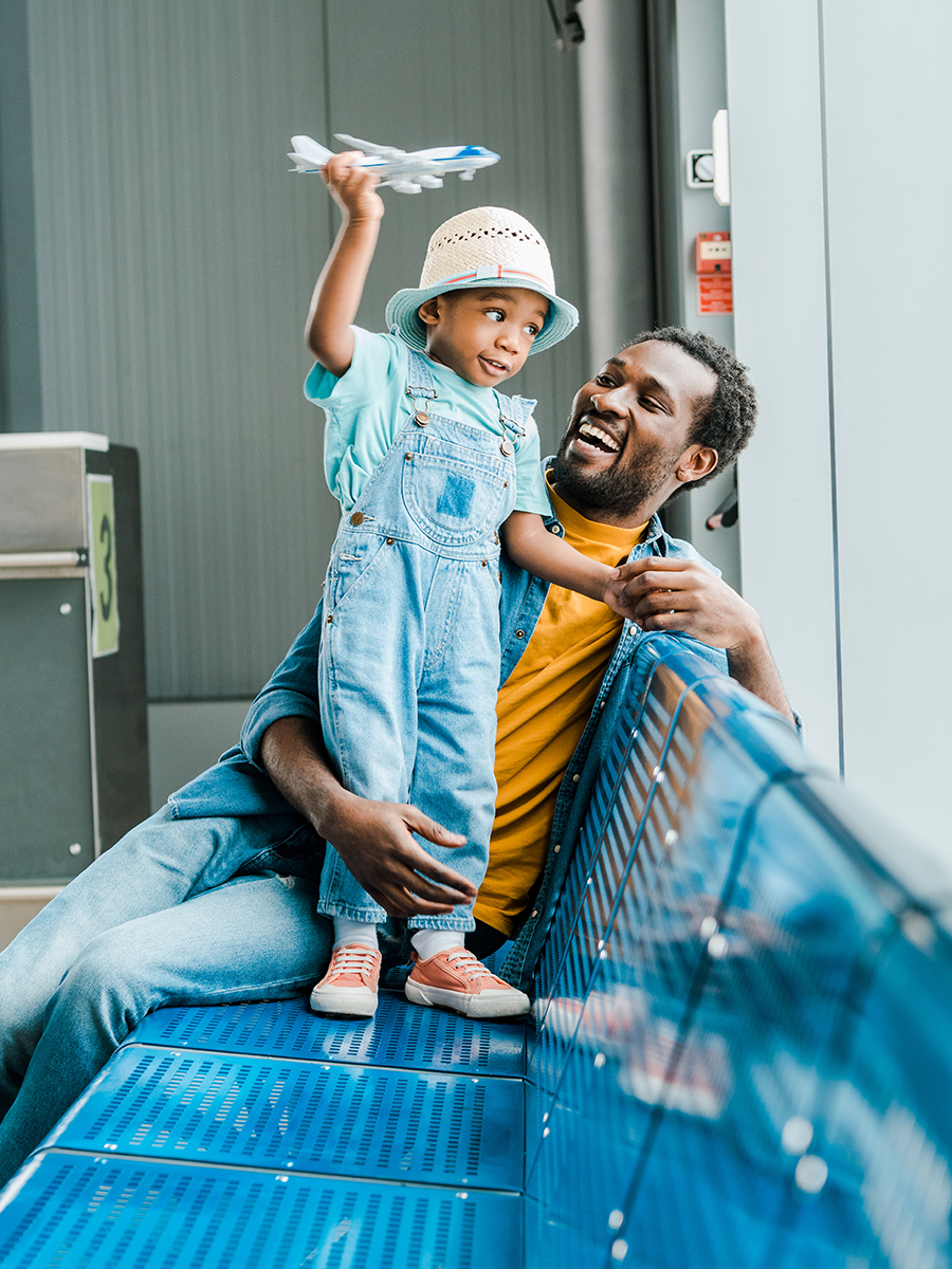 Male and toddler boy sitting on a bench with toddler holding a toy airplane