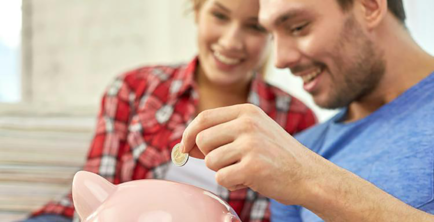 A couple dropping a coin into a pink piggy bank.