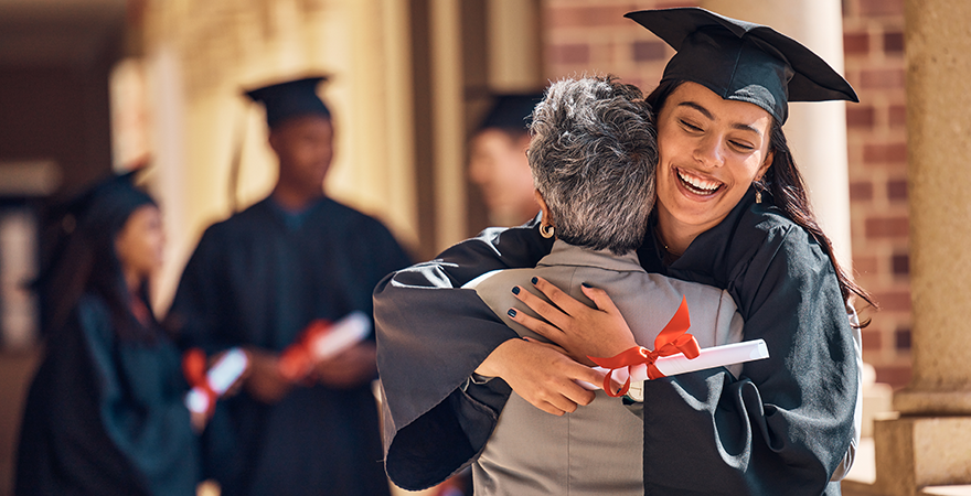 A graduate in cap and gown hugging an older man at a graduation ceremony.